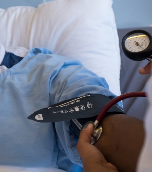 An African male patient lies in bed while the female medical doctor checks at his blood pressure